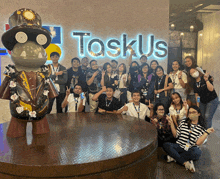 a group of people posing for a picture in front of a sign that says taskus