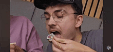 a man is eating sushi with chopsticks and wearing glasses .