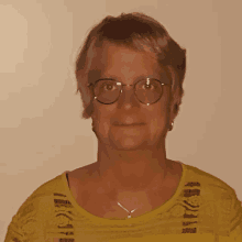 a woman wearing glasses and a yellow shirt is smiling for the camera