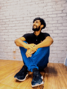 a man with a beard sits on the floor with his legs crossed and looks up