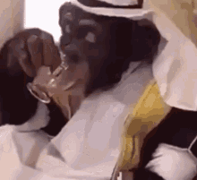 a chimpanzee is drinking from a glass while wearing a turban and a hat .