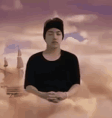 a man is meditating in the clouds while wearing a black shirt and a beanie .