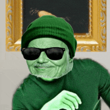 a green man wearing sunglasses and a green hat stands in front of a framed picture