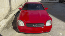 a red mercedes is parked in a parking lot next to a wall