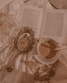 a cup of coffee , a mirror , a book , and a necklace are on a bed .