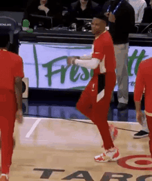 a man in a red shirt is dancing on a basketball court with other players .