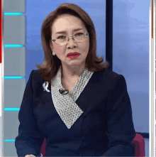 a woman wearing glasses and a black jacket is sitting in front of a blue wall