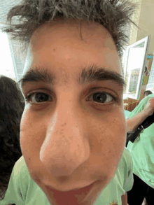 a close up of a young man 's face with a large nose and a green shirt .