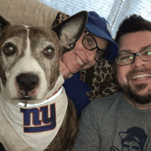 a dog wearing a ny bandana poses for a picture with a man and woman