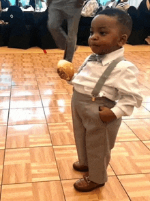 a little boy wearing suspenders and a bow tie holds a piece of bread