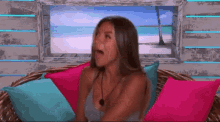 a woman is sitting on a couch with her mouth open and a beach in the background .