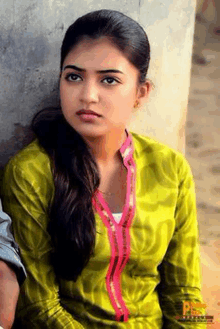 a woman in a green shirt is leaning against a wall and looking at the camera