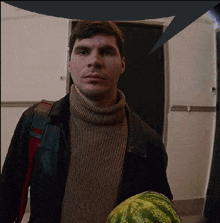 a man in a turtleneck sweater holds a watermelon