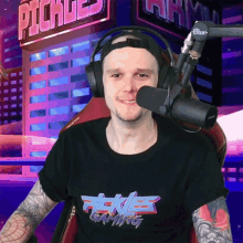 a man wearing headphones and a pickles gaming shirt smiles in front of a microphone