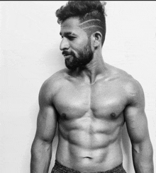 a shirtless man with a beard and mohawk is standing in front of a white wall .