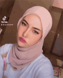 a woman wearing a pink hijab is taking a selfie with a tiktok logo in the background