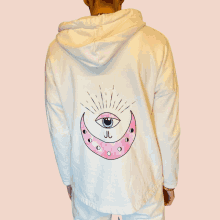 a person is wearing a white hoodie with a pink crescent moon and an eye on it