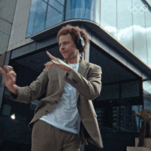 a man in a suit and headphones is dancing in front of a building with the olympic symbol on it