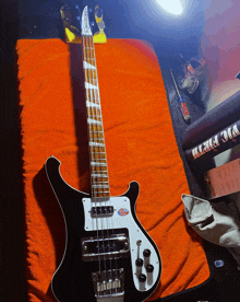 a rickenbacker bass guitar sits on an orange blanket