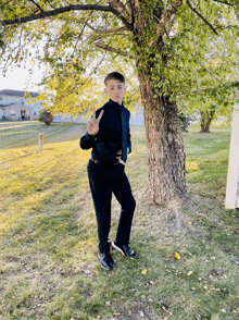 a young man in a suit and tie stands in front of a tree giving the peace sign