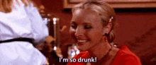 a woman is smiling and saying `` i 'm so drunk '' while sitting at a bar .