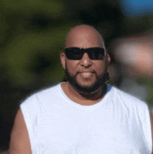 a man with a beard wearing sunglasses and a white tank top