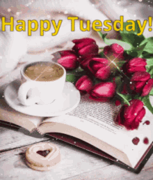 a cup of coffee is sitting on top of an open book next to a bouquet of red tulips .