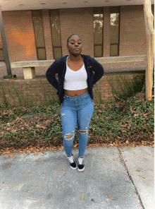 a woman wearing ripped jeans and a white crop top stands on a sidewalk