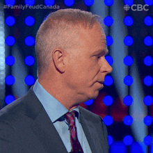 a man in a suit and tie is standing in front of a blue background with the words family feud canada on it