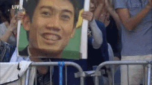 a man is holding a picture of a man 's face in front of a crowd of people .