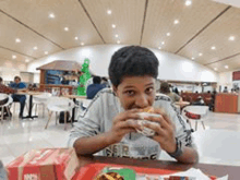 a young boy is eating a hamburger at a restaurant .