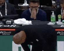 a man sits at a sports boston table with his hands on his face