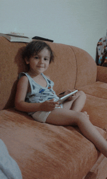 a young boy sits on a couch holding a cell phone