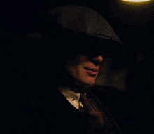 a man wearing a hat and tie is looking at something in the dark