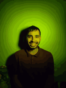 a man with a beard is smiling in front of a green wall