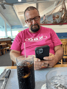 a man wearing a pink t-shirt that says obx is looking at his phone