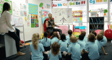 a group of children are sitting on the floor in a classroom with a man dressed as thor sitting in front of them