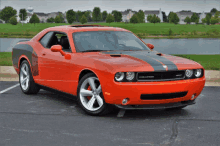 an orange dodge challenger is parked in a parking lot near a body of water