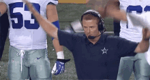 a man wearing headphones and a shirt with a star on it stands in front of a group of cowboys players