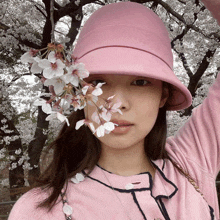 a woman wearing a pink hat is holding a bunch of flowers in front of her face