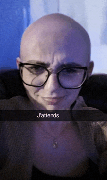 a bald woman wearing glasses and a necklace with a caption that says j'attends