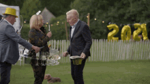 a man in a suit stands next to a woman holding a tray of champagne glasses and a man in a yellow hat