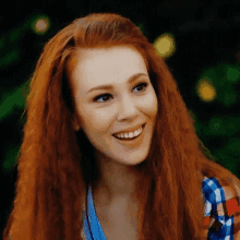 a woman with long red hair is smiling and wearing a blue shirt