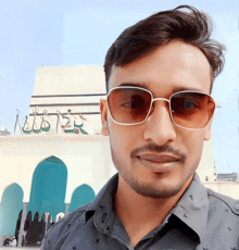 a man wearing sunglasses stands in front of a building that has the word allah on it