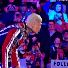 a man in a red and blue outfit is standing in front of a crowd and a sign that says follow