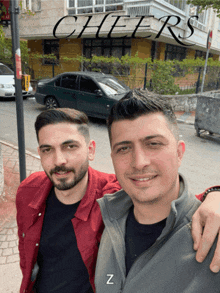 two men are posing for a picture in front of a sign that says " cheers "