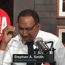 a man wearing glasses and a name tag that says stephen a. smith is sitting in front of a microphone