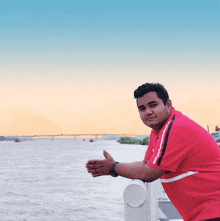 a man in a red shirt with the word puma on it leans against a railing overlooking a body of water