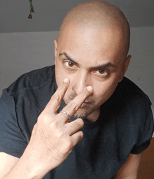 a bald man with a ring on his finger holds his hand to his nose