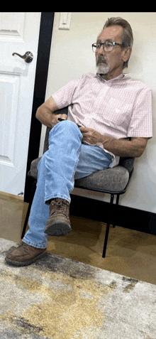 a man in a pink shirt and jeans sits in a chair